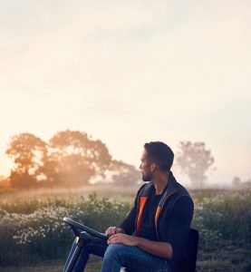 Un utilisateur profite d’un moment calme au lever du soleil avec un rider HUSQVARNA, conçu pour une tonte précise et confortable des grandes pelouses.