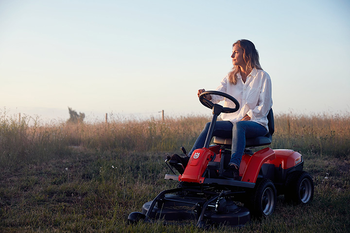 Utilisatrice conduisant un rider HUSQVARNA dans une prairie pour tondre la pelouse avec une tondeuse autoportée.